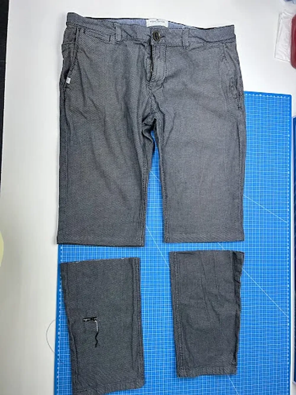 A shortened pair of trousers beside the cut-off legs on the cutting mat